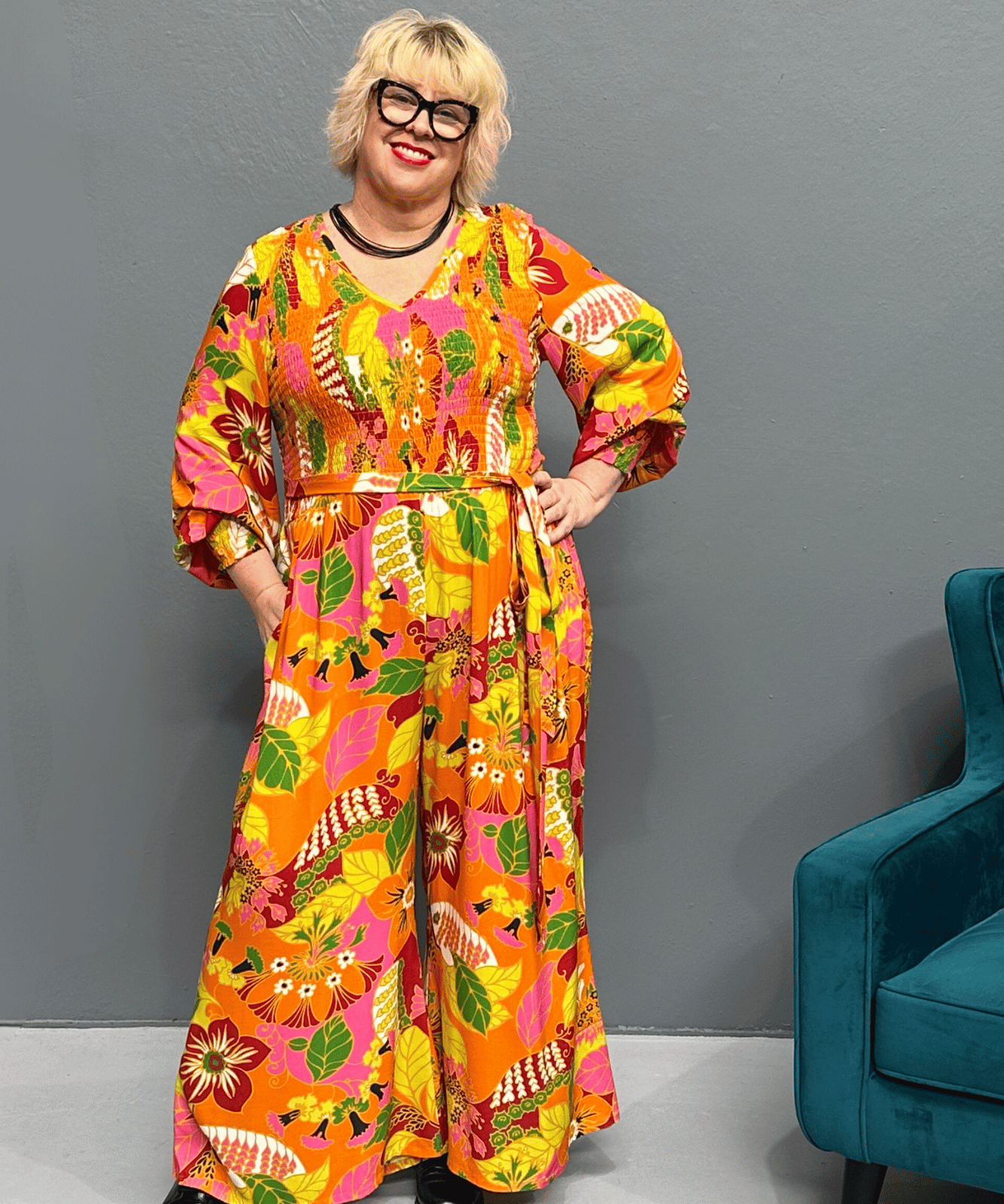 Plus-size 'FEARLESS' jumpsuit in retro print with pink, orange, and golden yellows, featuring a relaxed wide-leg cut and flattering shirred bodice.