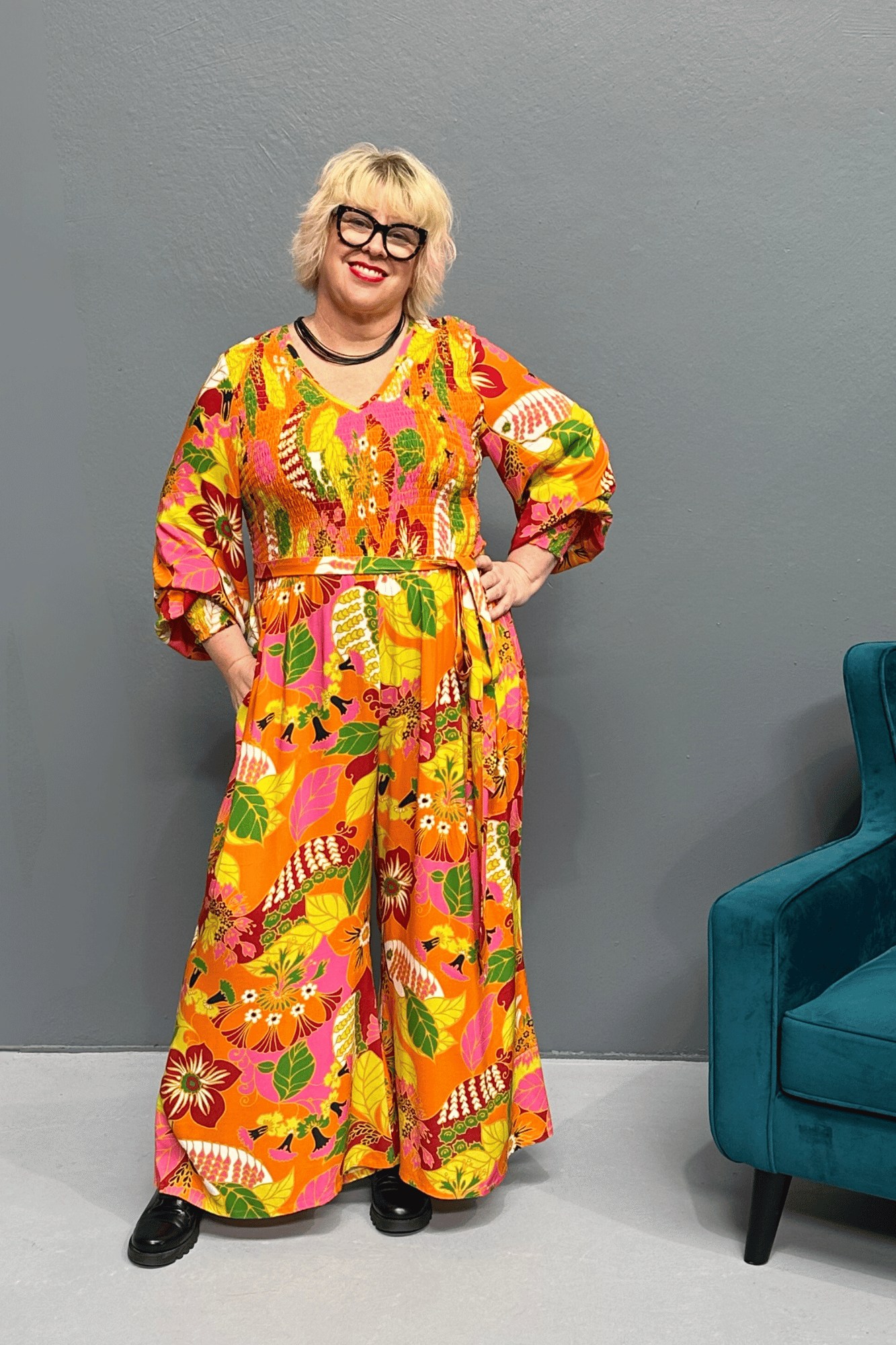 Plus-size 'FEARLESS' jumpsuit in retro print with pink, orange, and golden yellows, featuring a relaxed wide-leg cut and flattering shirred bodice.