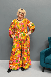 Plus-size 'FEARLESS' jumpsuit in retro print with pink, orange, and golden yellows, featuring a relaxed wide-leg cut and flattering shirred bodice.